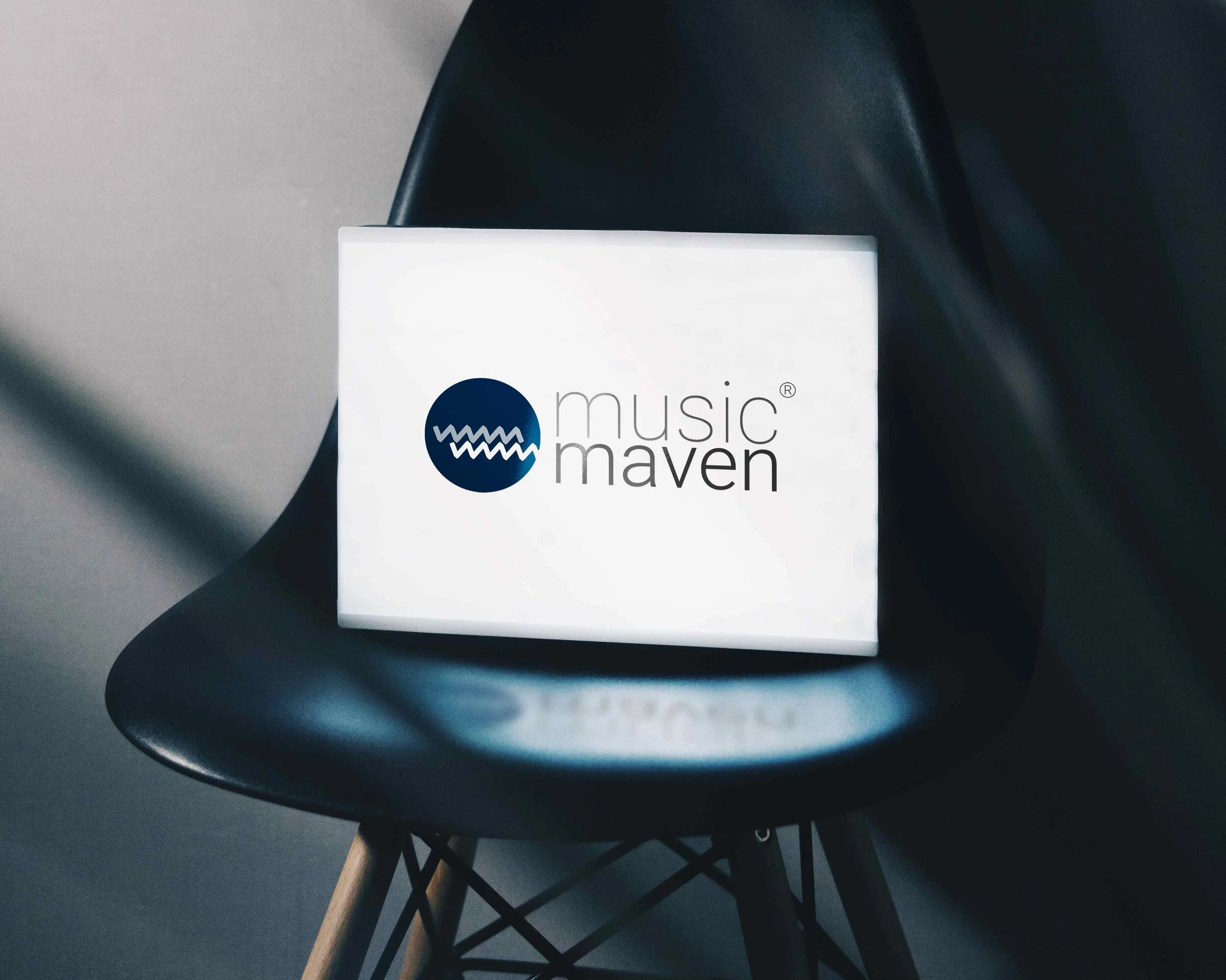 A white illuminated box displaying the logo and text 'music maven' hangs on a black chair.