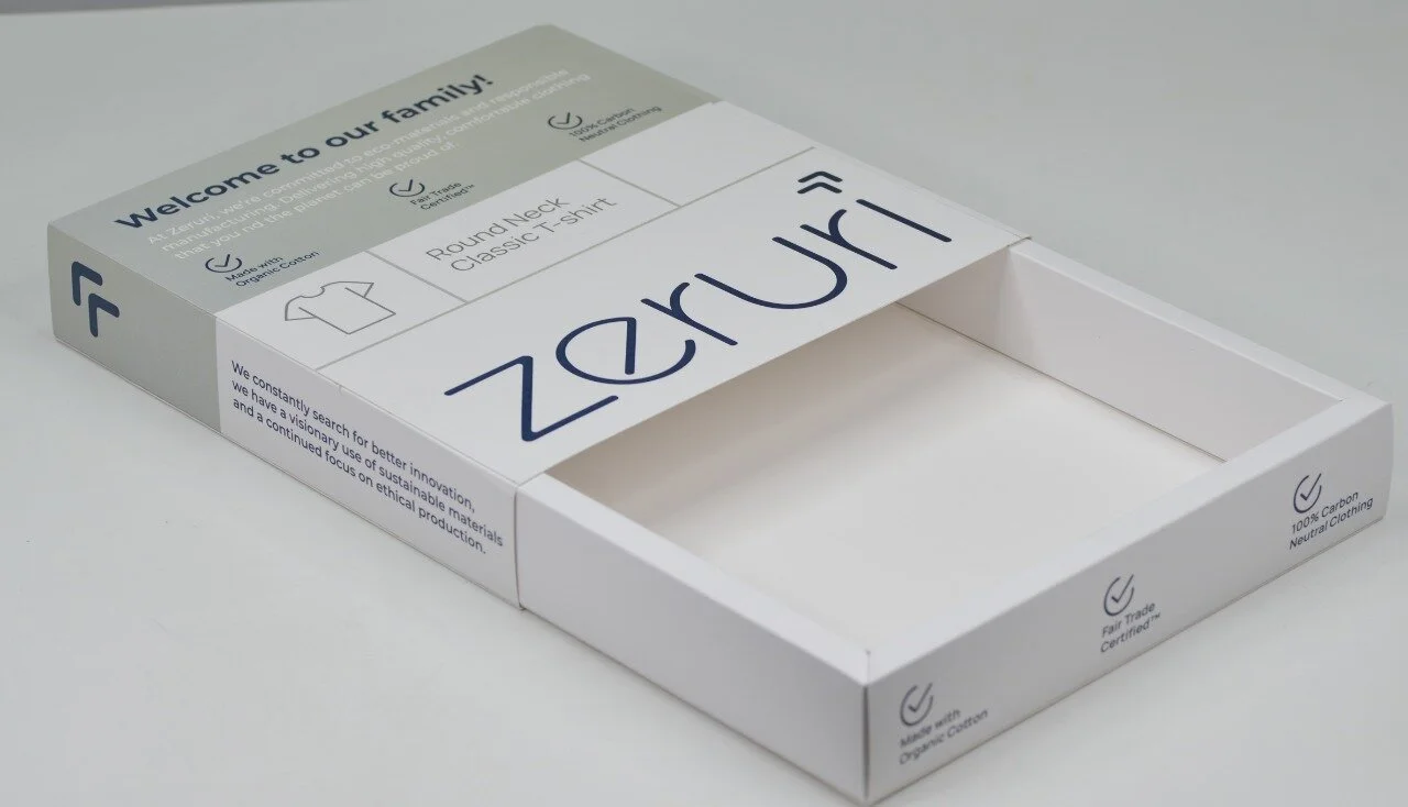 Open white packaging box with branding for Zeruri, an eco-friendly clothing company, featuring labels indicating 100% carbon neutral clothing, fair trade certified, and made from organic cotton.