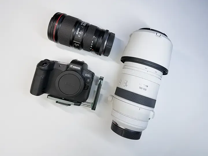 Camera with large white telephoto lens and another smaller black lens on a white surface
