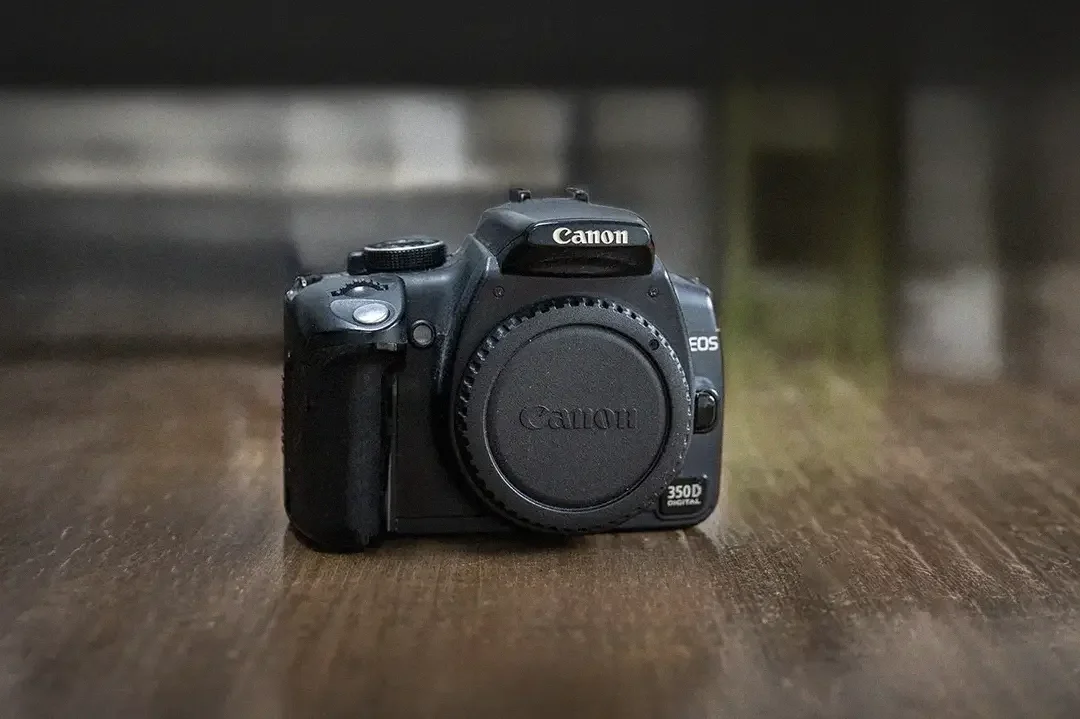 A black Canon EOS 350D digital camera on a wooden surface with a blurred background.