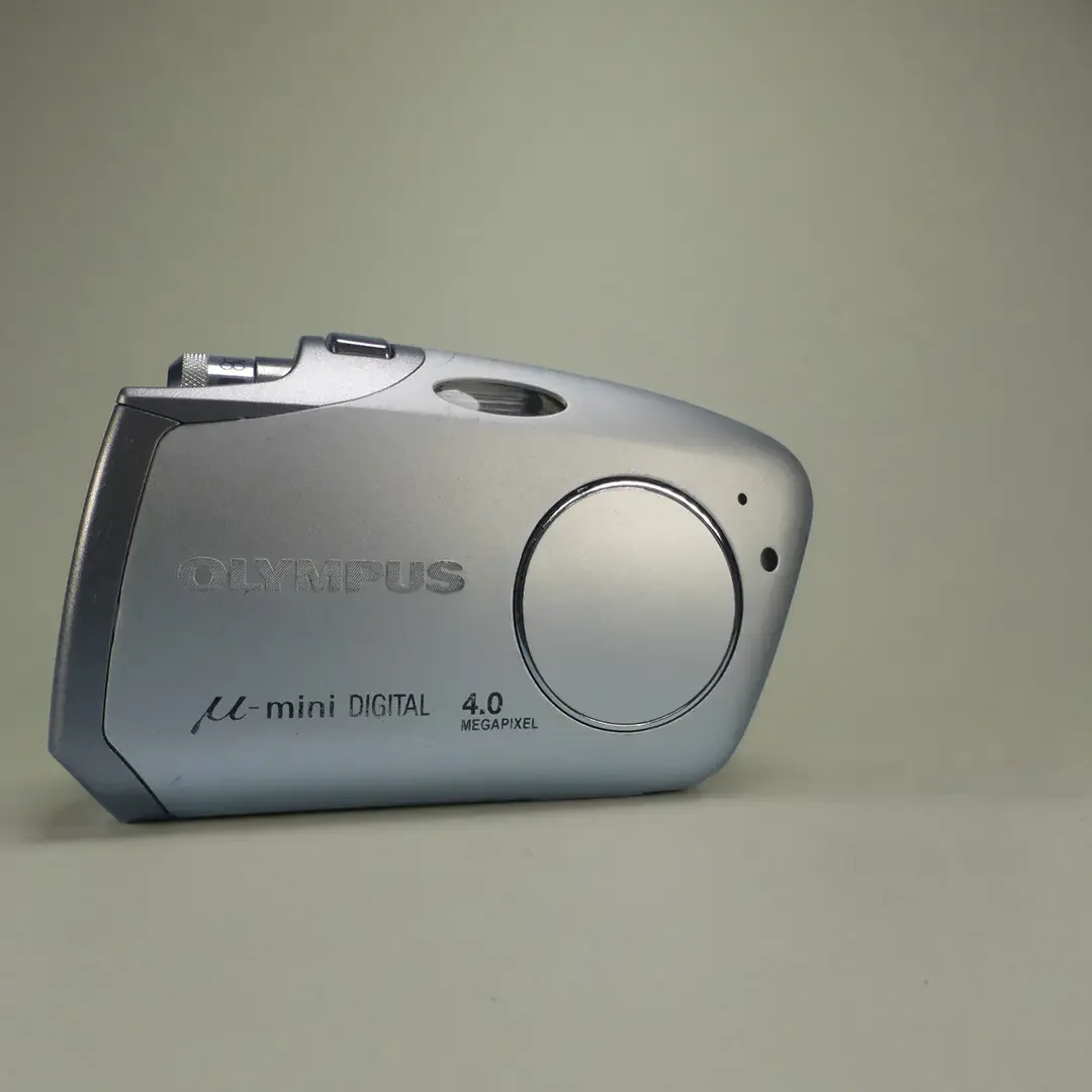 Silver Olympus digital compact camera with a large circular lens area, placed on a plain background.