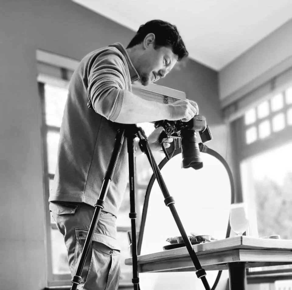 A man setting up a camera on a tripod in a room with large windows.