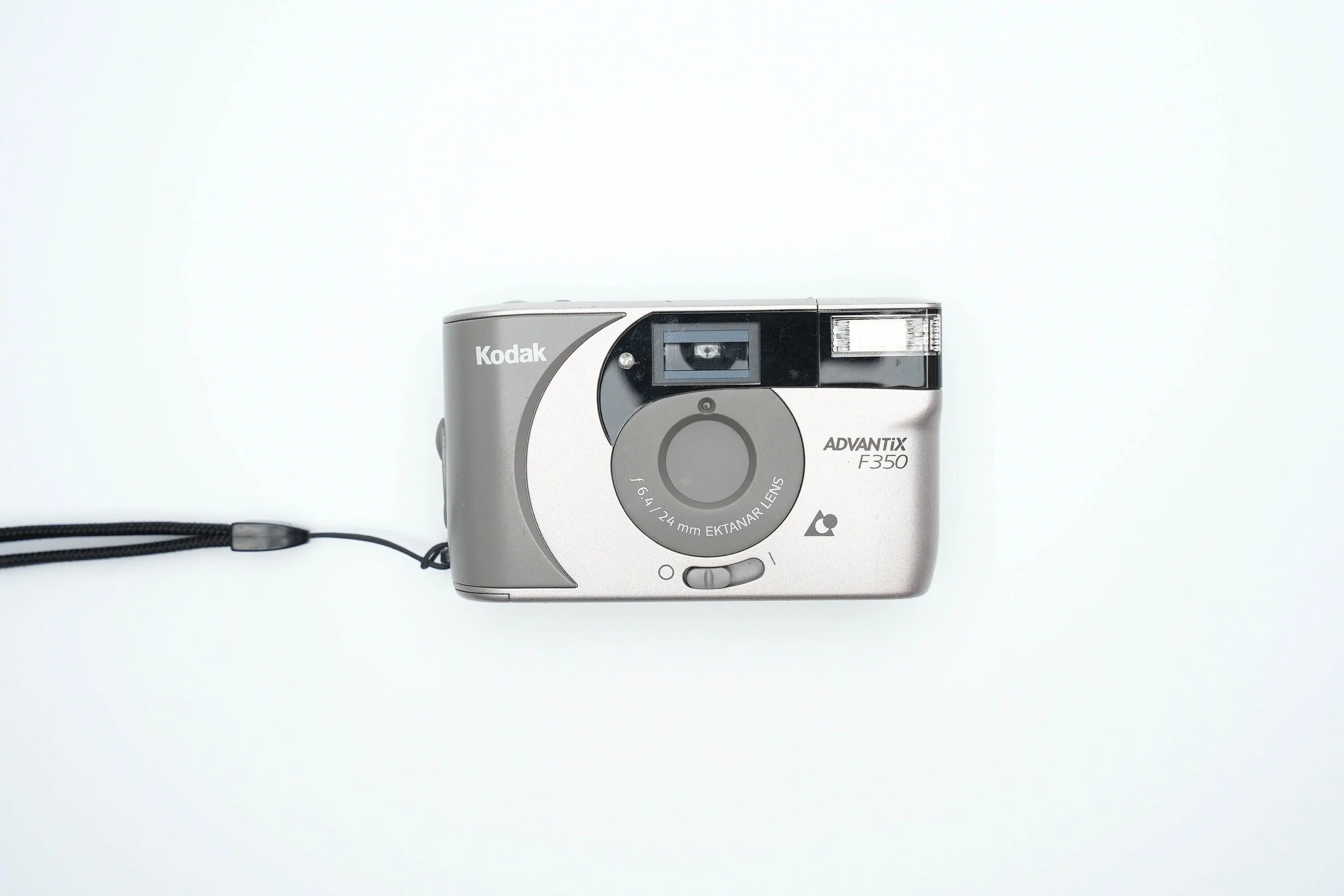 Silver Kodak Advantix F350 camera with black and gray accents, facing upward on a white background, with a black wrist strap extending from the left side.