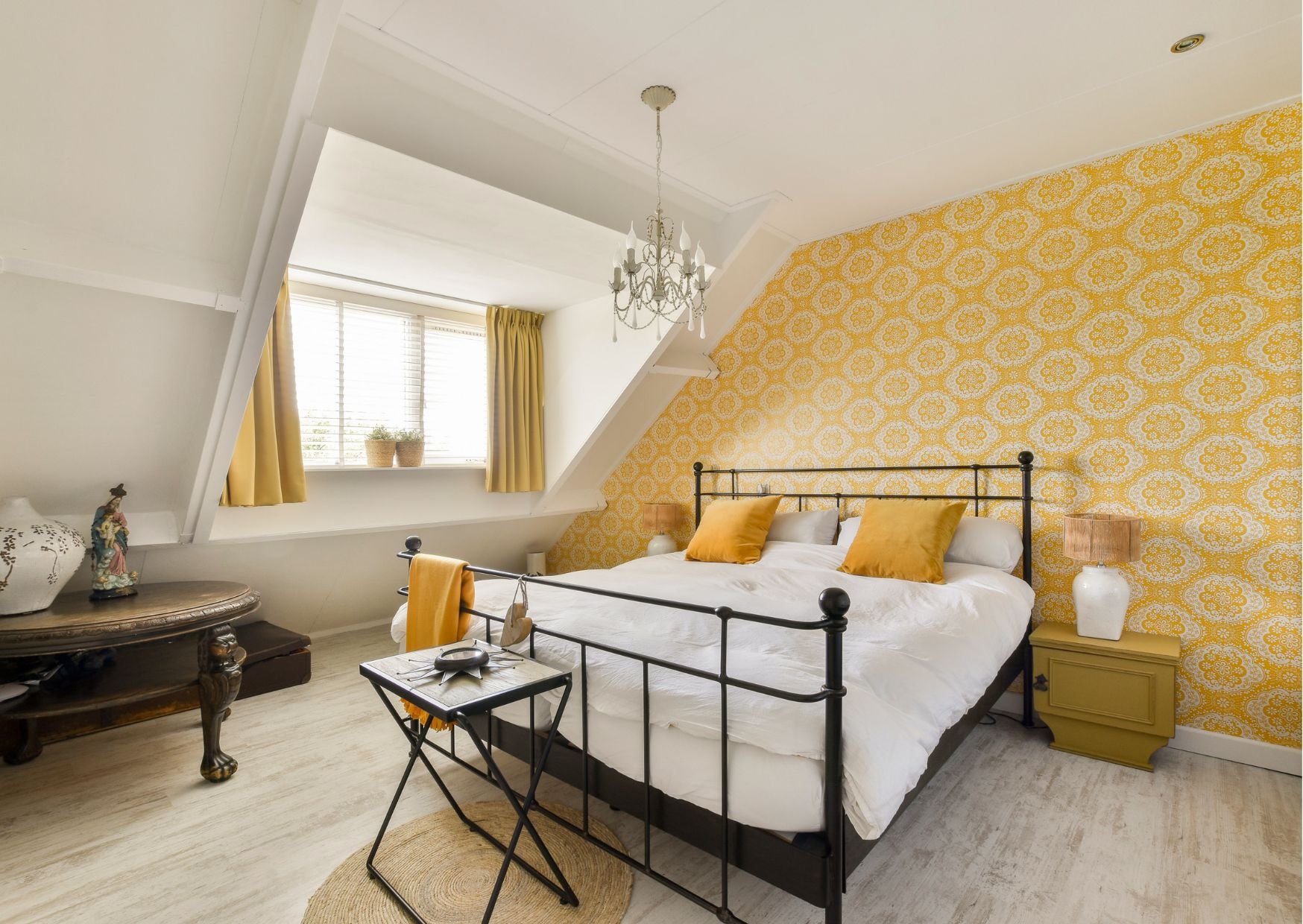 Charming attic bedroom featuring bold yellow patterned wallpaper, black metal bed frame, chandelier, and sloped ceiling design. Image 8: