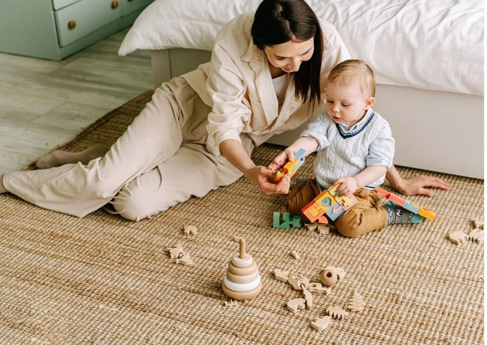 Parent and child playtime on a woven rug with wooden toys and puzzles.