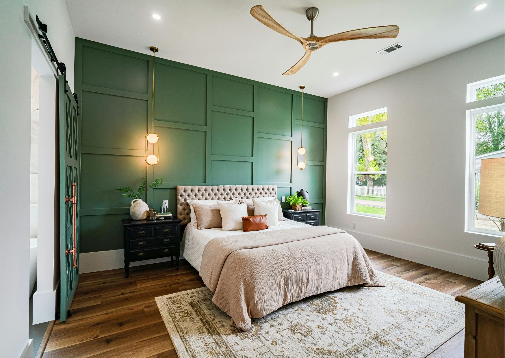 Contemporary bedroom with dark green paneled accent wall, tufted headboard, wooden floors, and natural light from large windows.