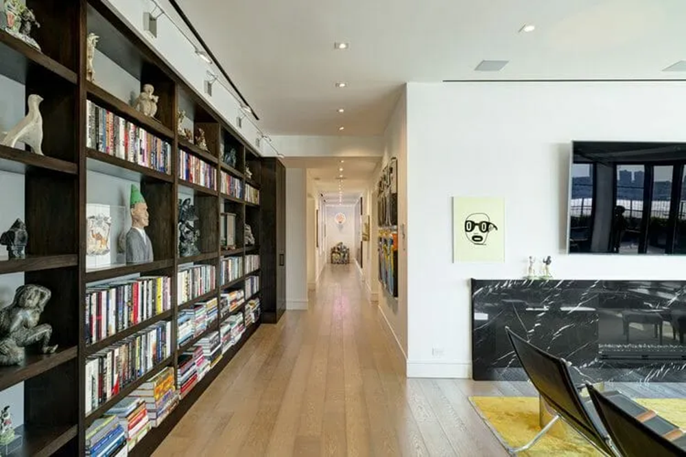 Modern living space with bookshelf, fireplace, artwork, and hallway lighting.