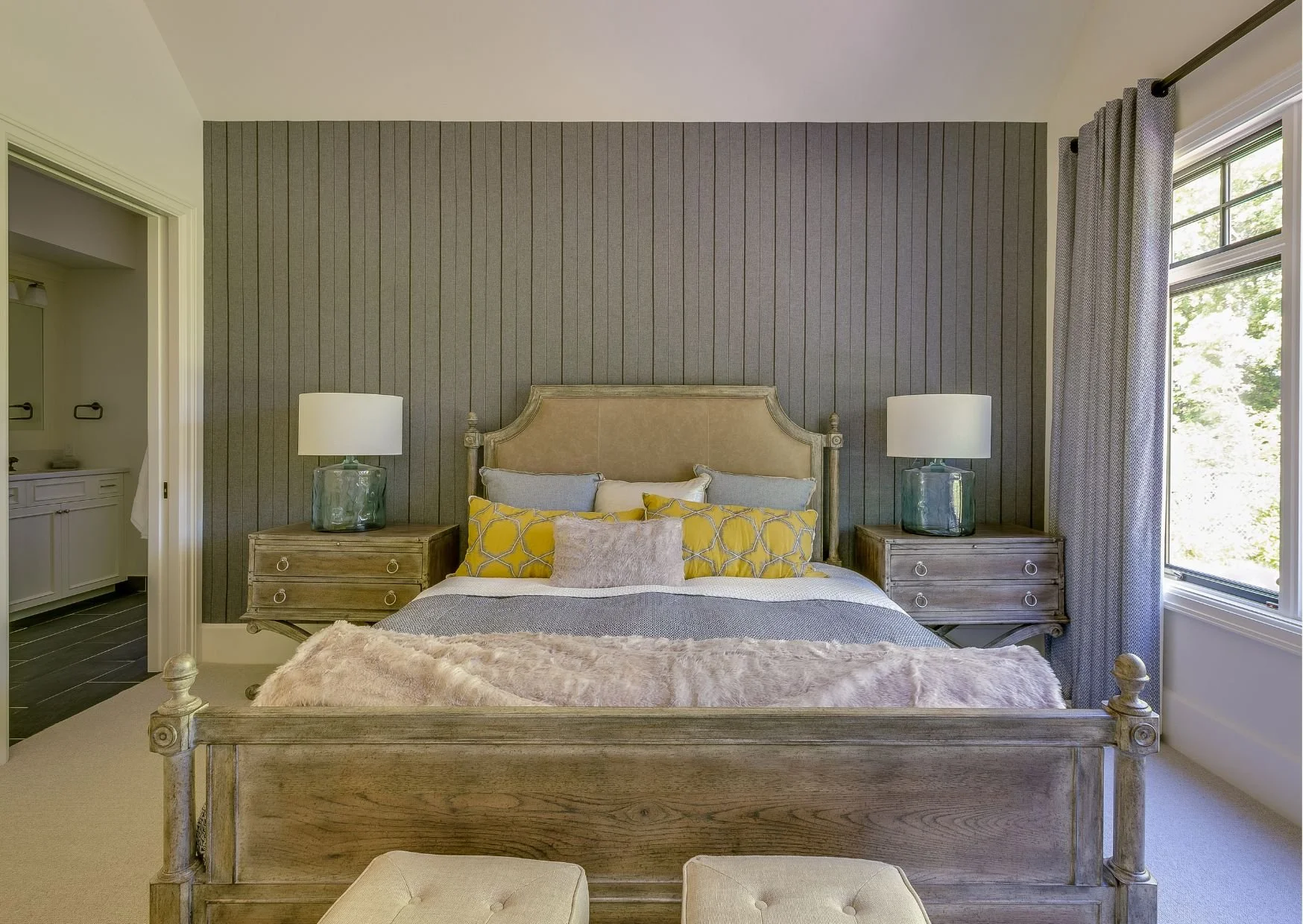 Cozy farmhouse bedroom featuring gray wood paneling, wooden bed frame, matching nightstands, and vibrant yellow decorative pillows.