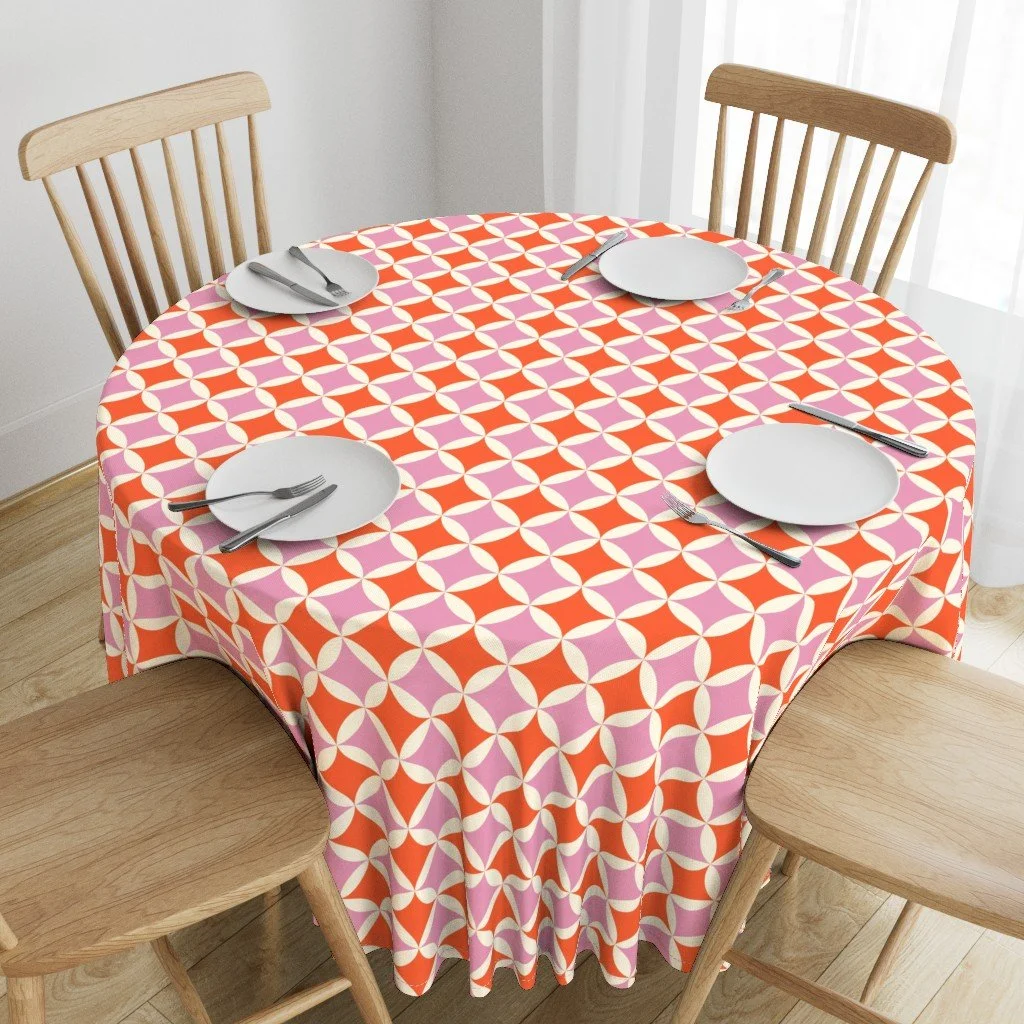Round tablecloth in a tangerine and pink orange peel geometric print, set with white plates, copyright Sandra Hutter.