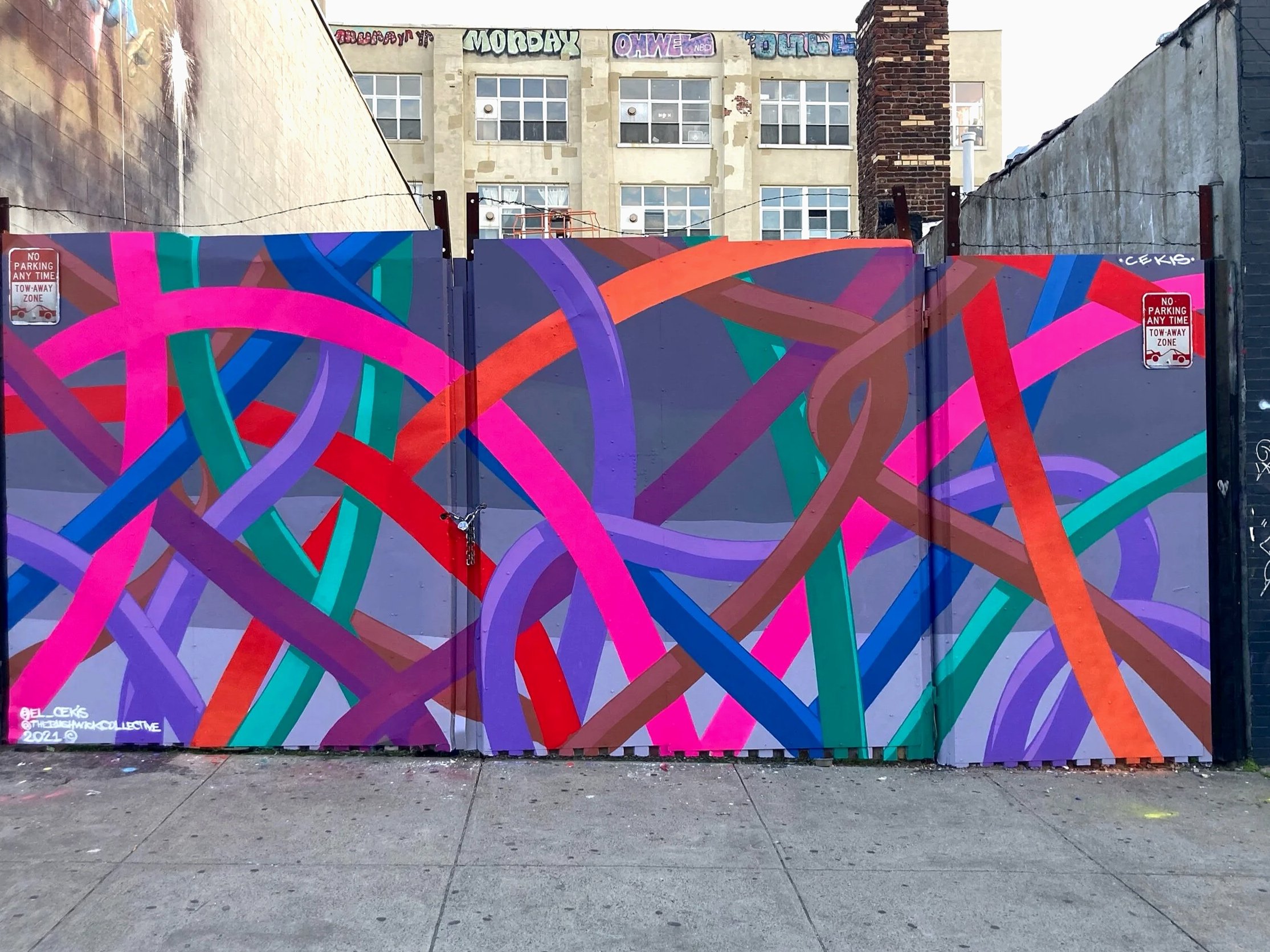 Colorful abstract graffiti mural with intertwining lines in pink, purple, blue, green, and brown on a metal fence.