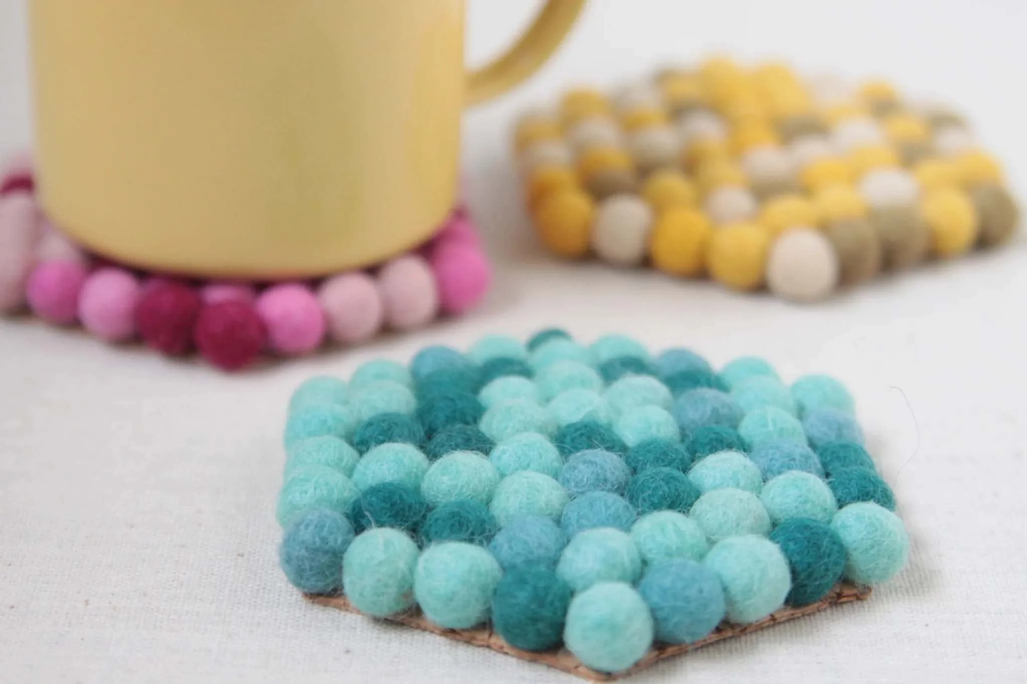 diy felt coaster made from felt balls in blue and yellow color with a cup on top of the coaster