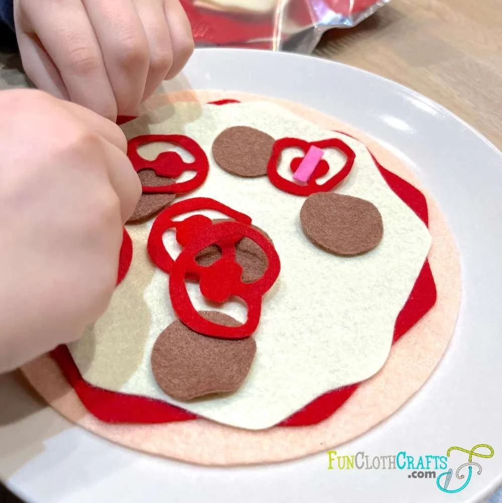 kid's hands playing with DIY felt pizza with pepperoni and tomatoes