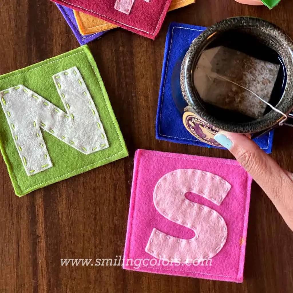 DIy felt coasters with letters in green and pink color and with a cup standing on the coaster