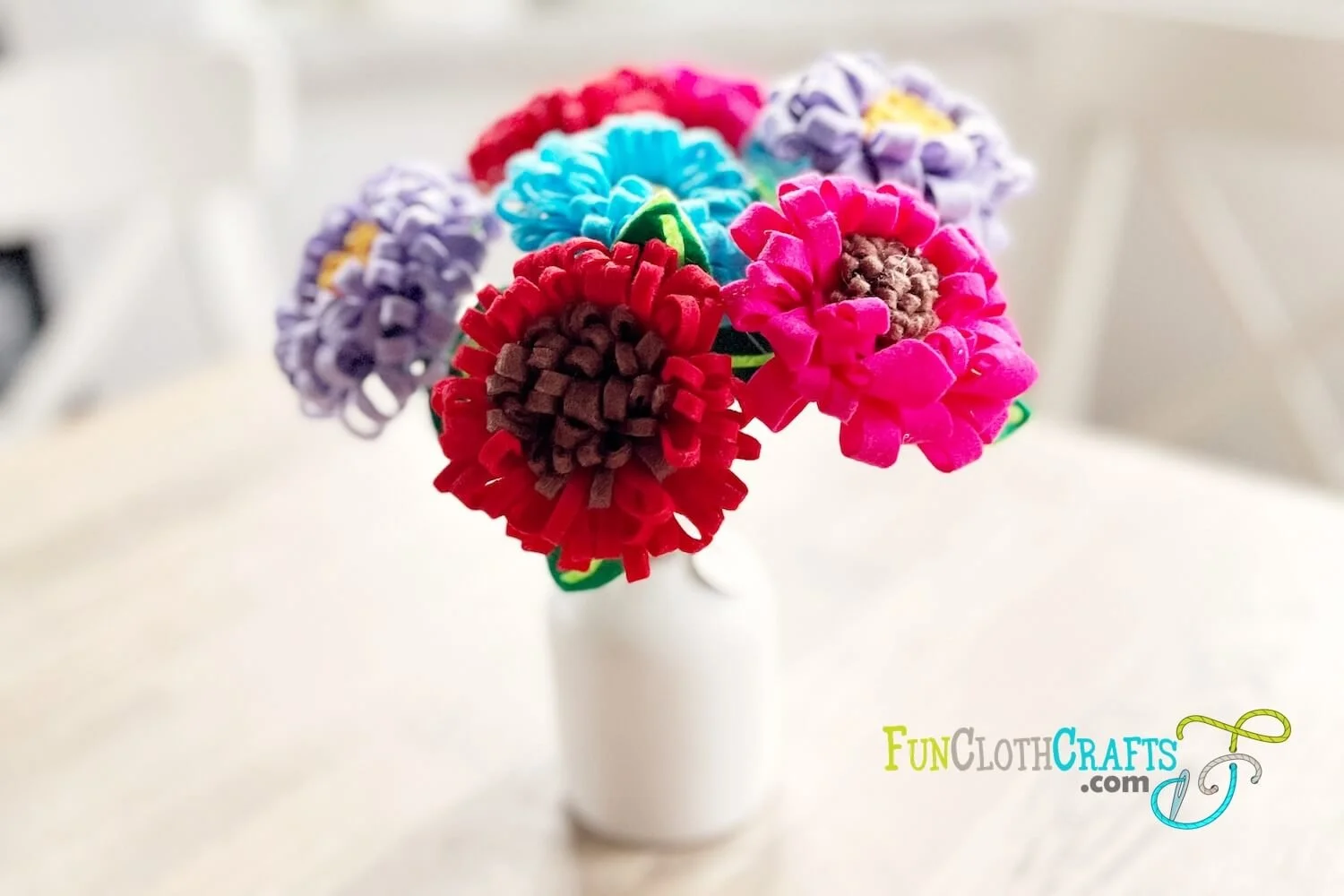 a bouquet of rolled felt flowers in a white vase