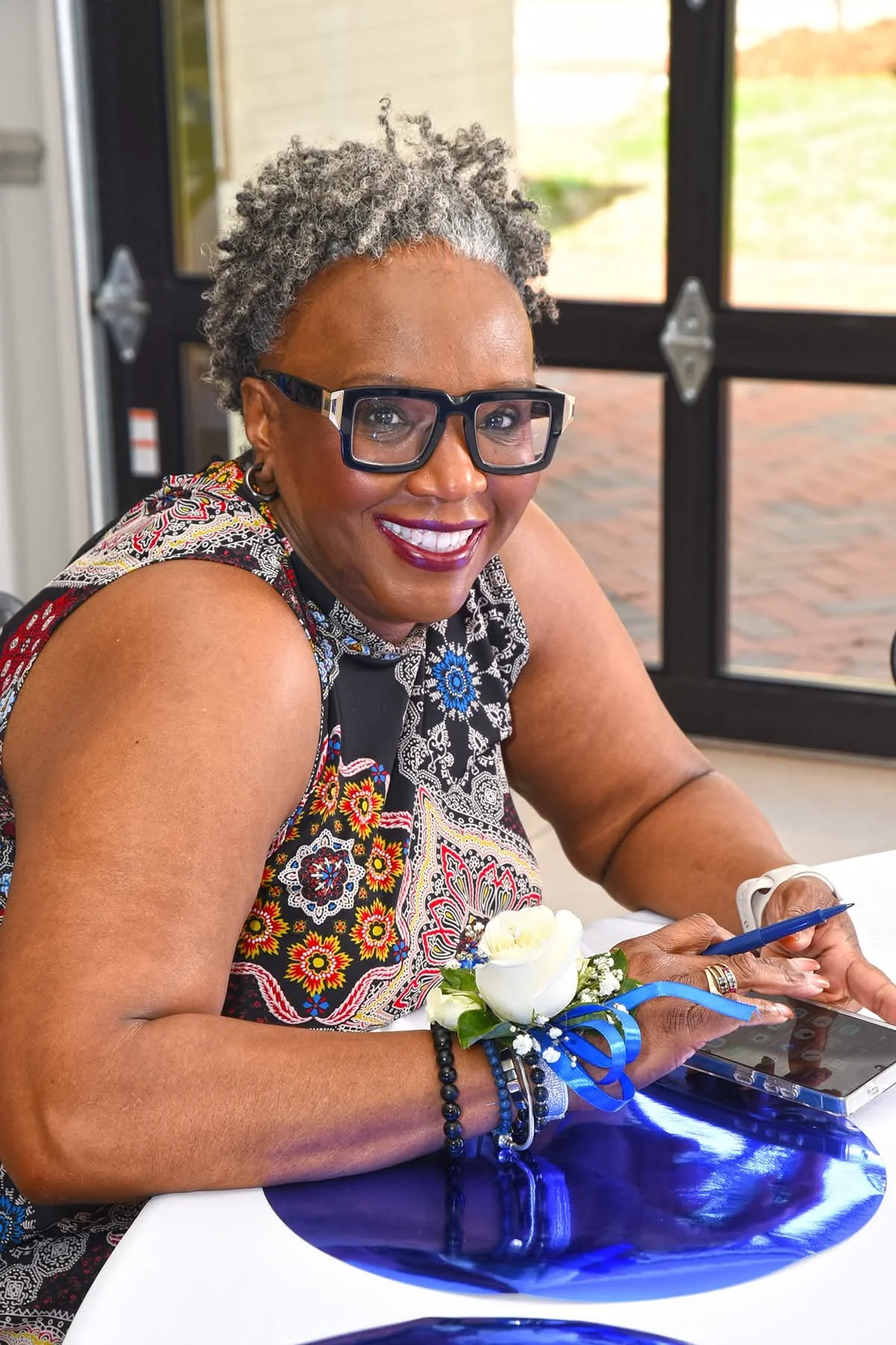 A person wearing dark glasses and a patterned shirt smiles in front of a door