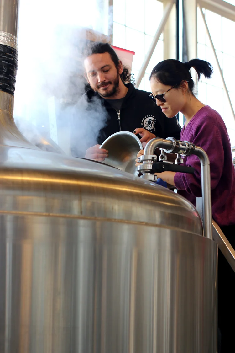 Two people looking into a steaming brewing tank