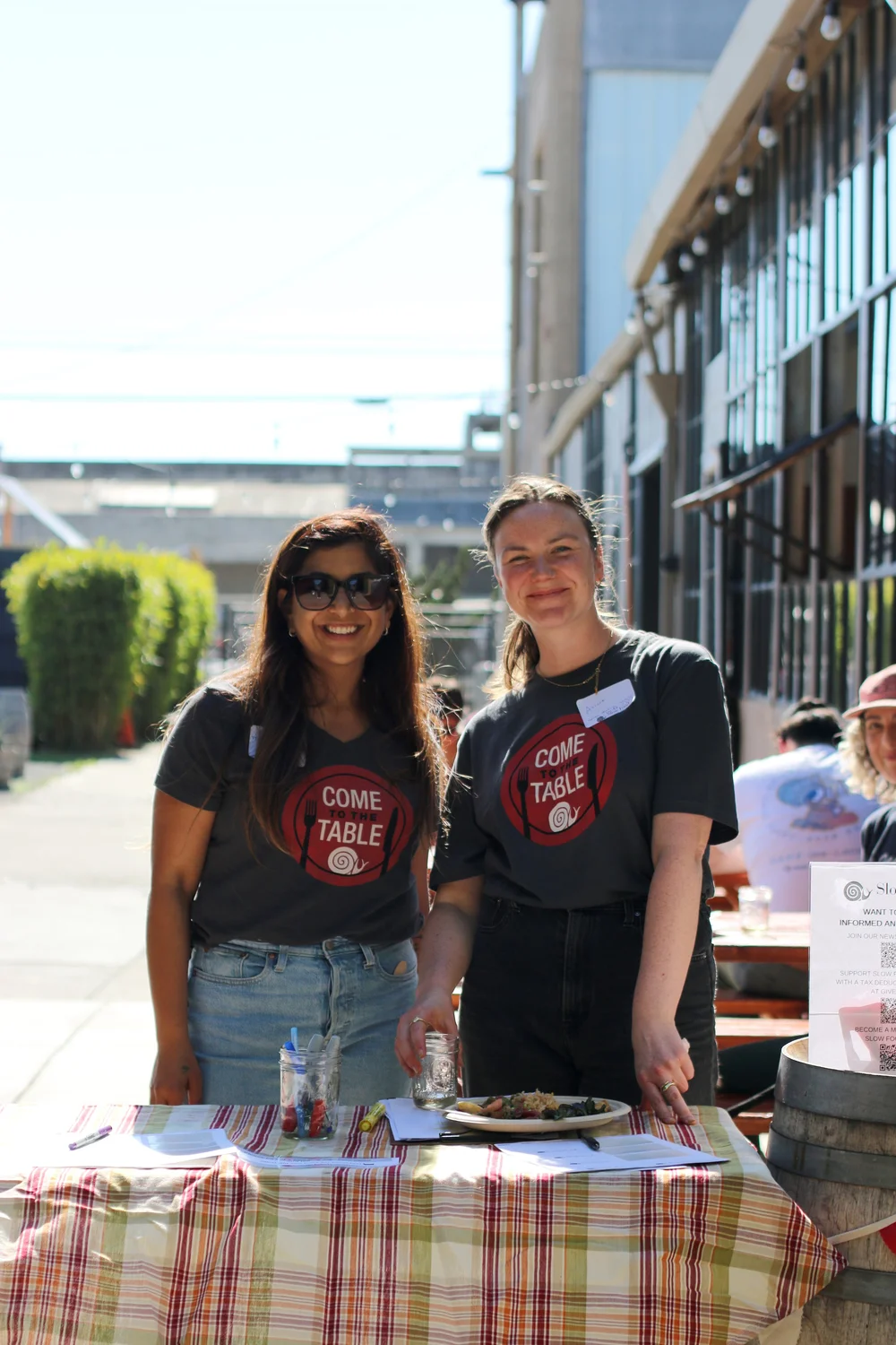 Two volunteers in Come to the Table shirts at an outdoor event table