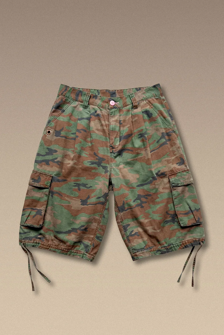 Washed camo canvas short with a relaxed, baggy fit. Fixed waistband with a pink button closure. Finished with side cargo pockets for utility and shape, and a pocket grommet to hang your keys.
