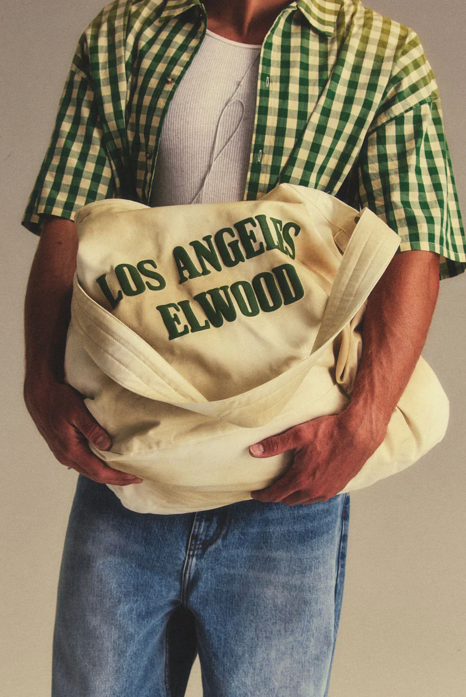 A vintage-inspired newspaper carrier, worn on the shoulder or crossbody. Made from canvas with an ink-worn finish and an Elwood Los Angeles graphic. Includes a thick strap, antique bronze button closure, and a roomy main compartment with an inner zip