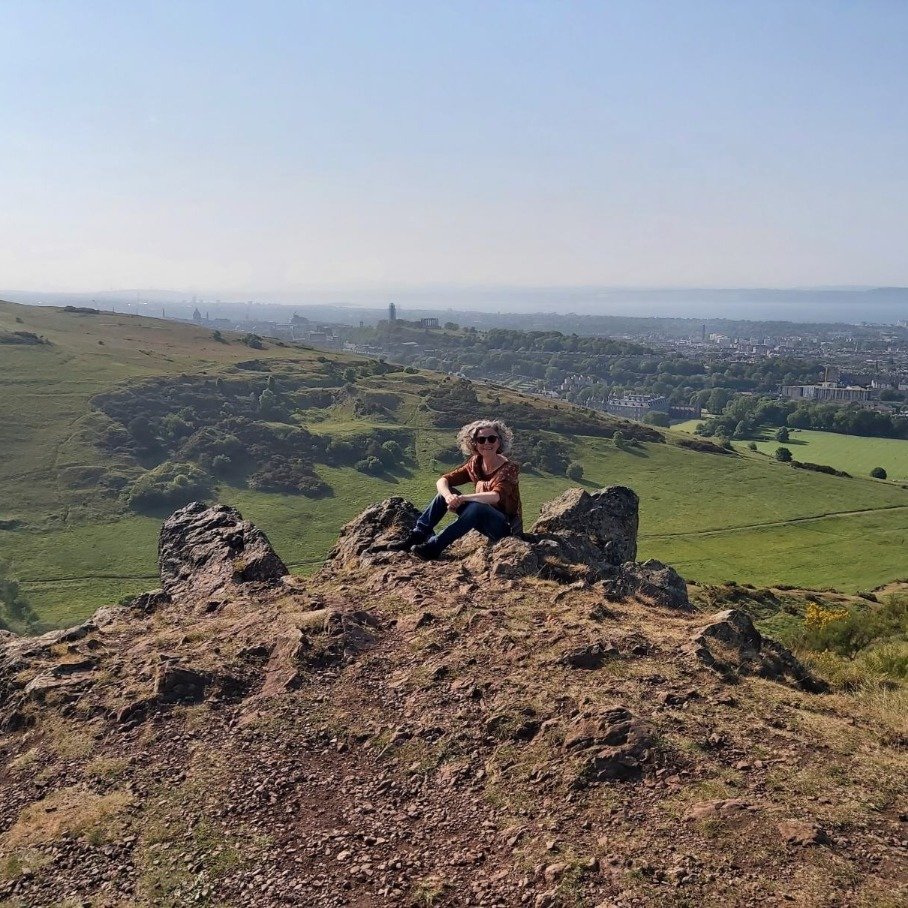 Jools on a hill in Scotland, smiling after walking for hours after her ME/CFS and POTS recovery.