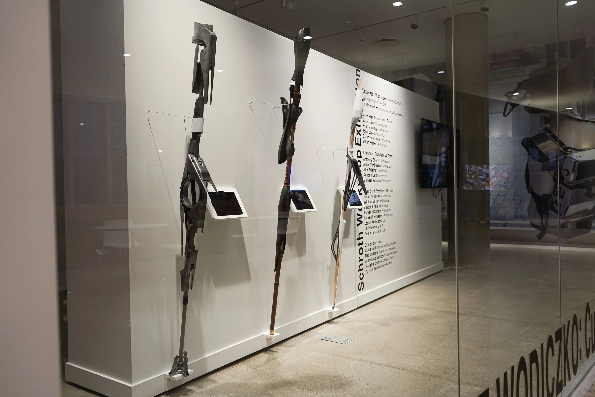 View of the Krzysztof's exhibit from the left side looking into the gallery featuring student project's on a white wall with ipads