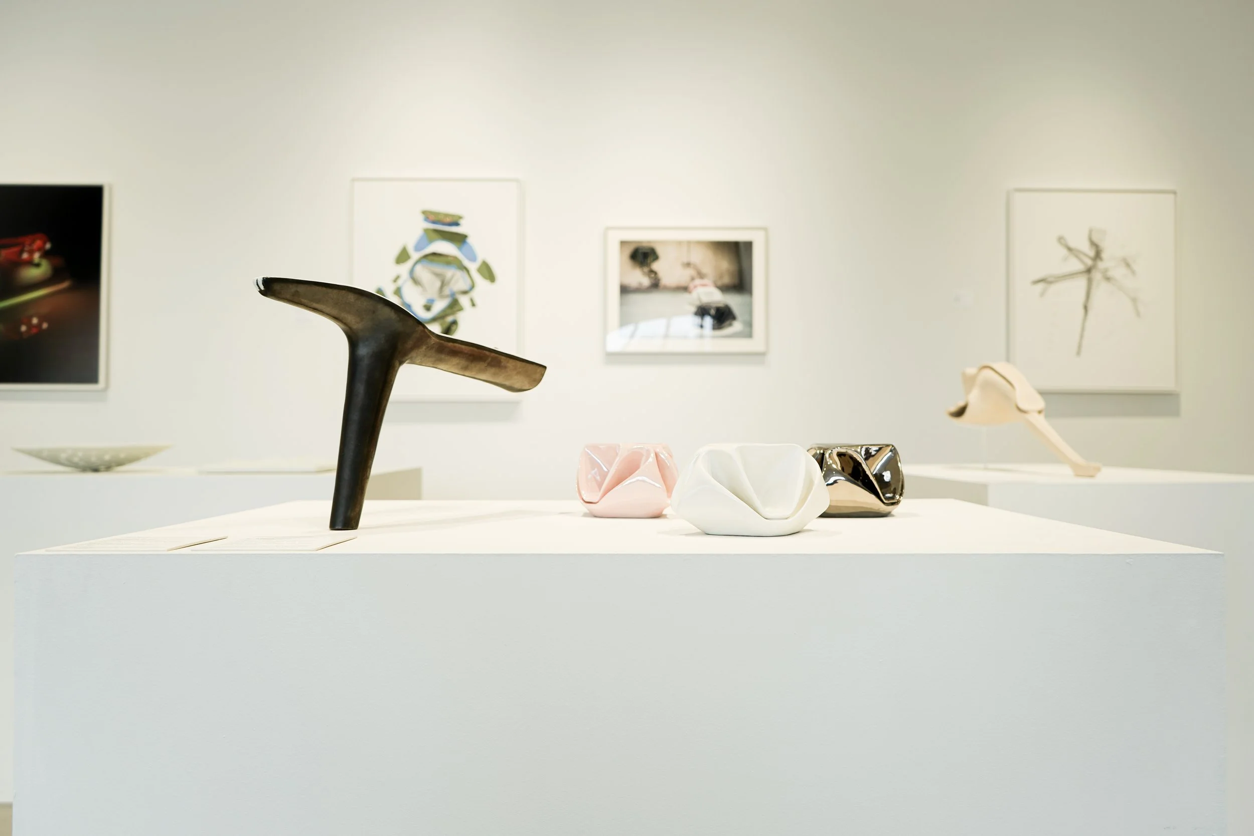 Ceramicology exhibit showing three vessels in pink, gold, and white, and metal staff