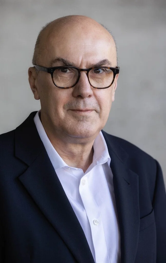 Bald man with brown glasses wearing a black blazer and white shirt