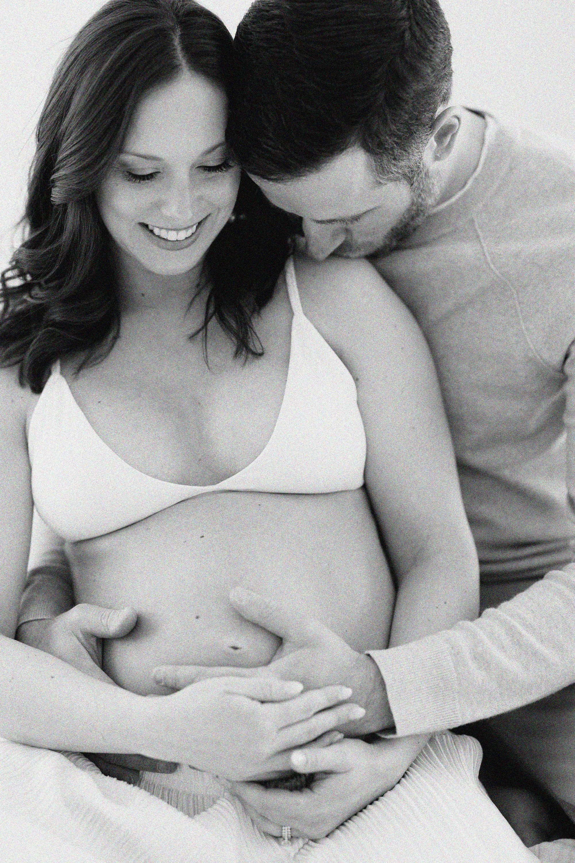 Expectant couple embracing with their hands gently resting on the mother's baby bump.