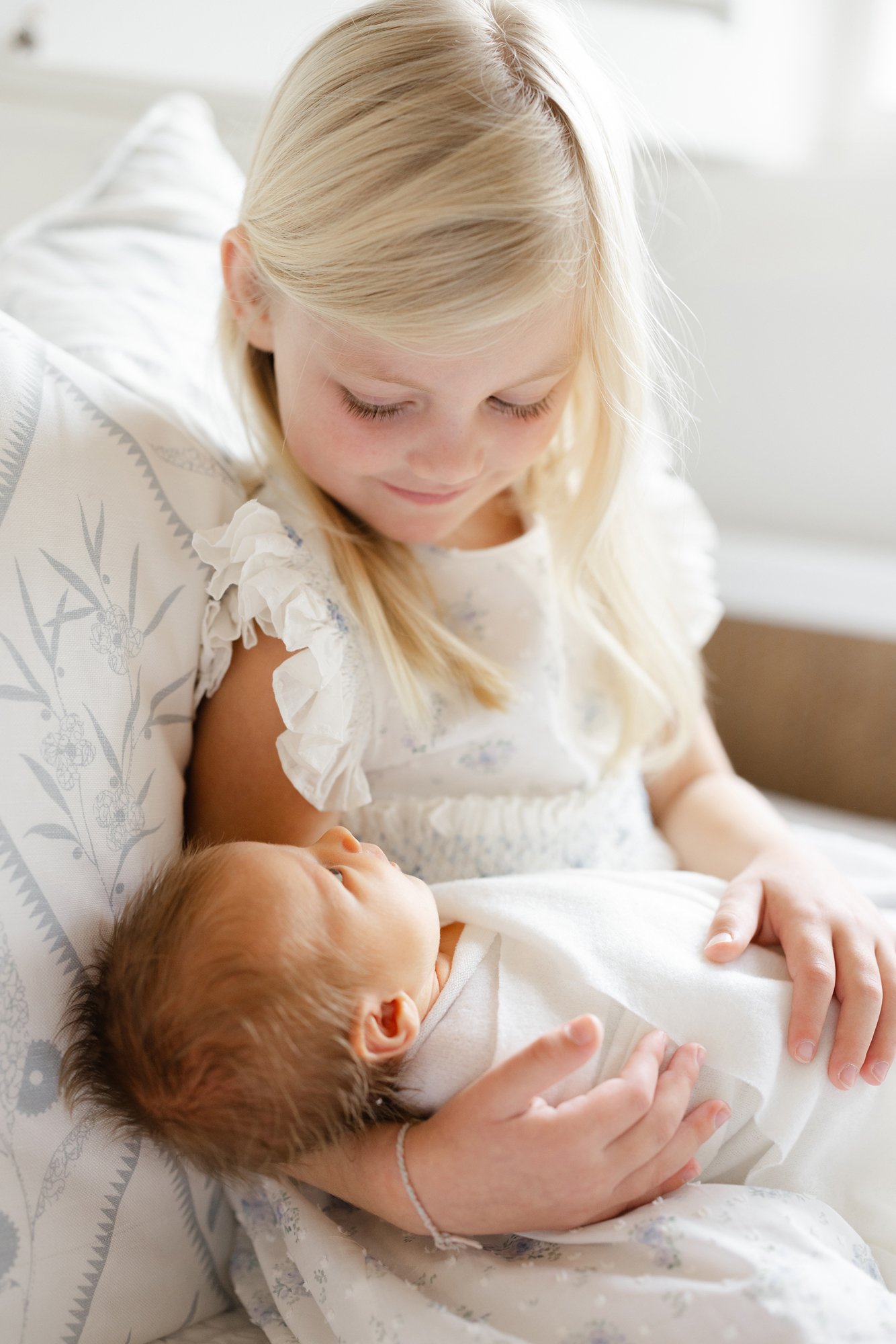 Older sister holding her newborn sibling during an in-home newborn photography session.