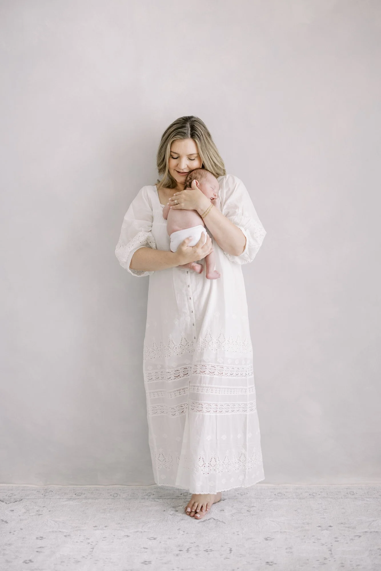 Mother standing while cradling her newborn during a minimalist studio newborn portrait.
