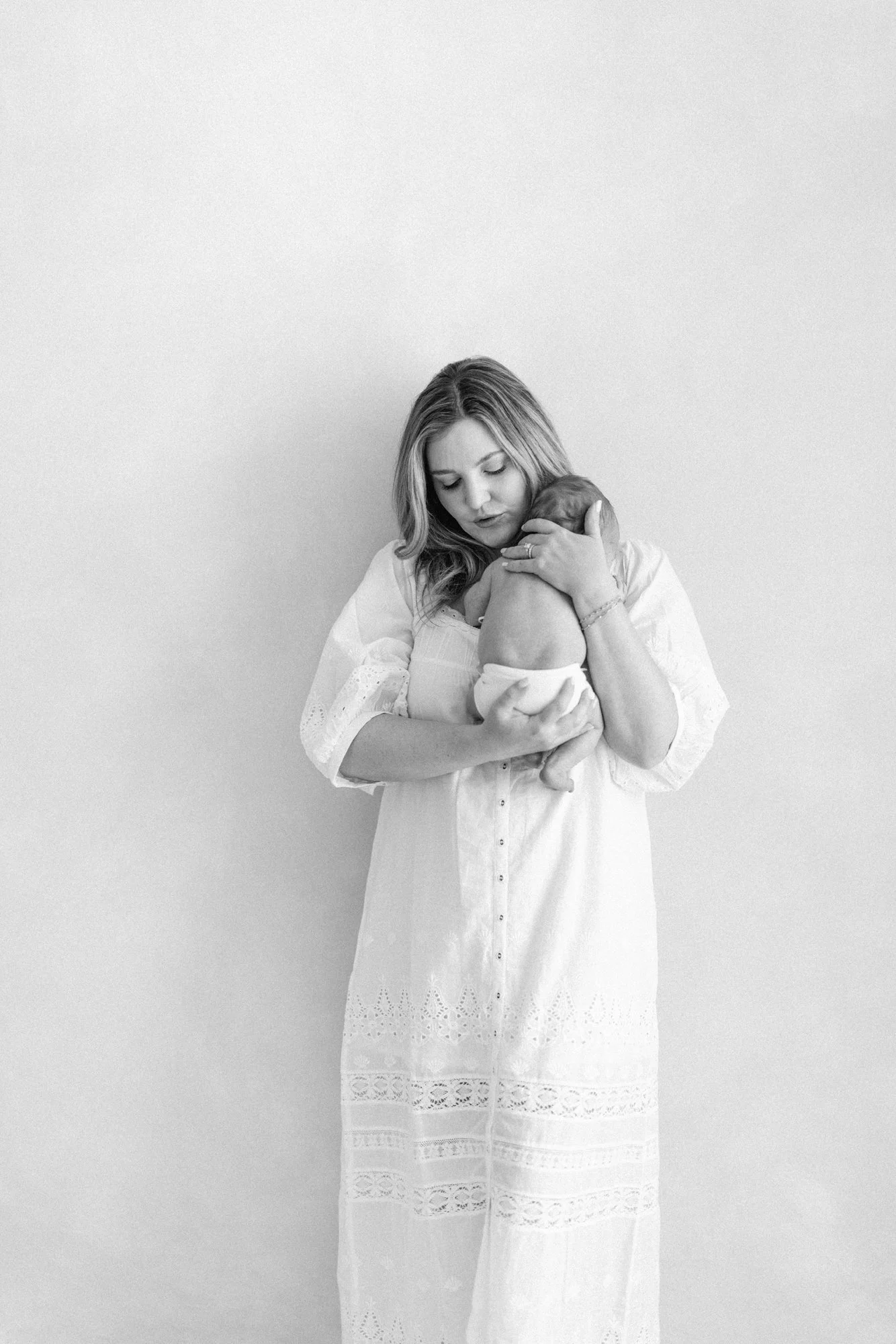 Black and white portrait of a mother standing and holding her newborn during a timeless studio session.