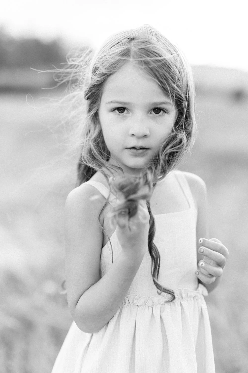 Black and white portrait of young girl twirling her hair during family portrait