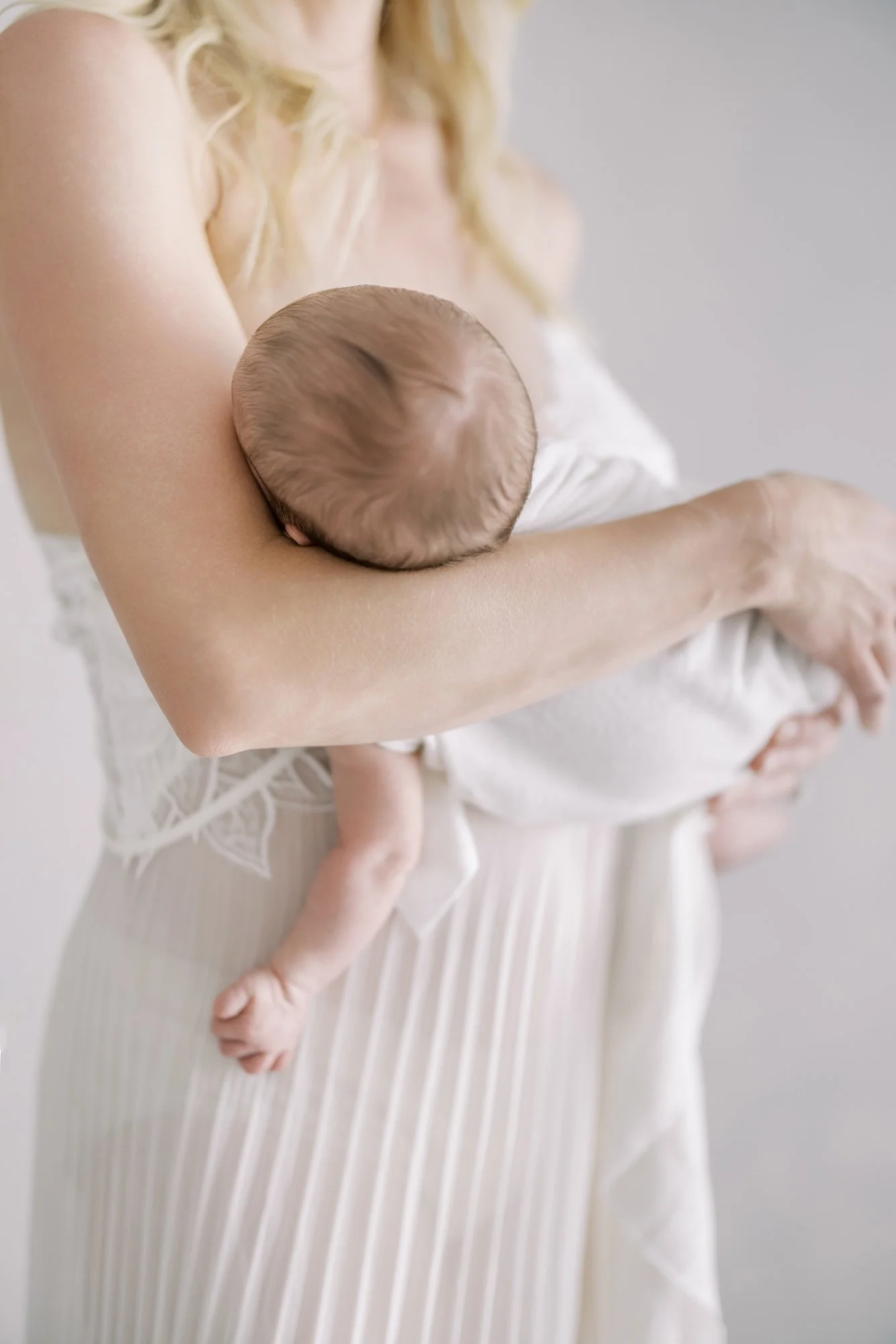 Close-up portrait of a mother cradling her newborn in her arms during a minimalist studio newborn session.