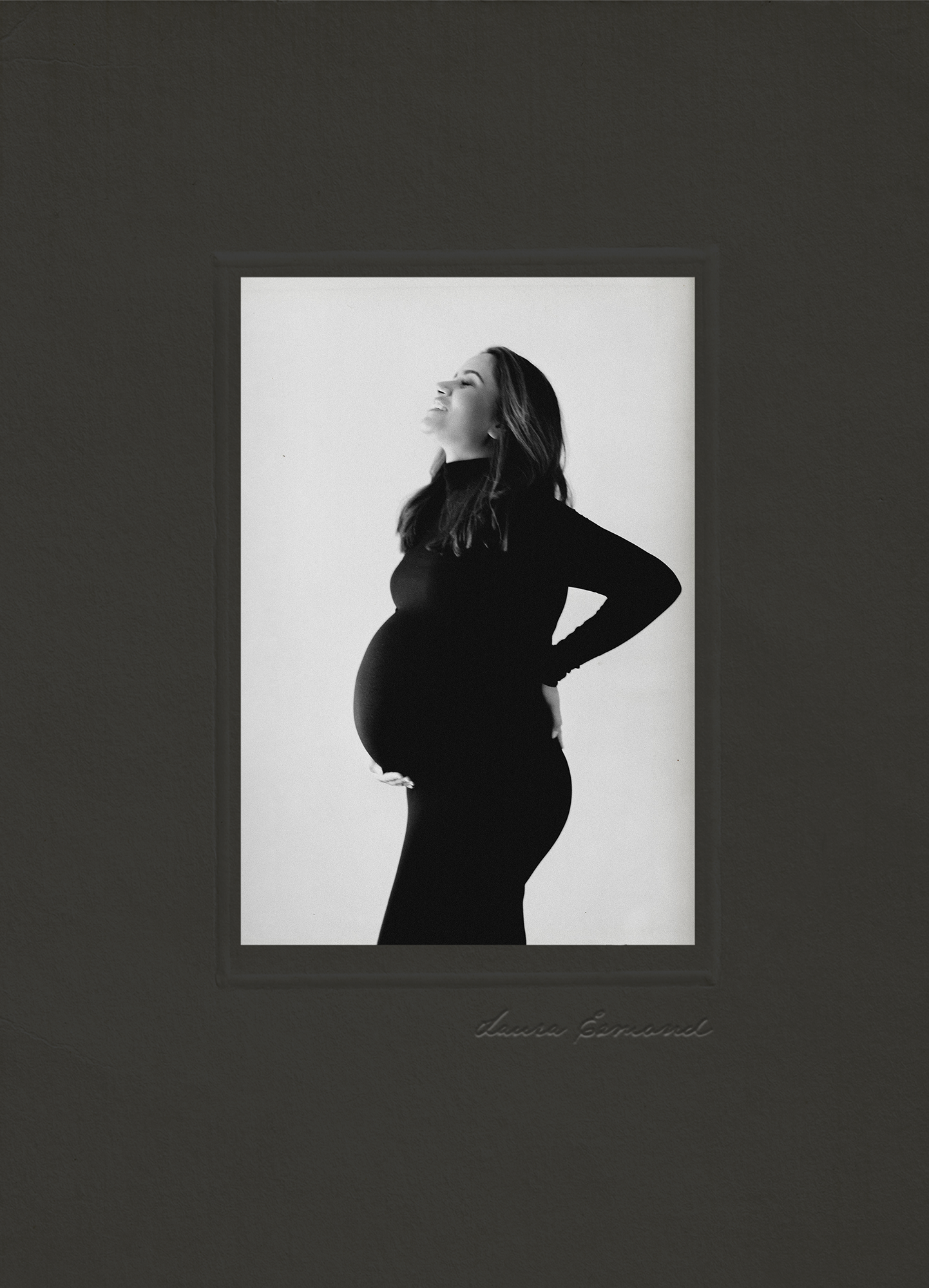 Pregnant mother smiling in profile while wearing a fitted black dress during a minimalist studio maternity portrait.