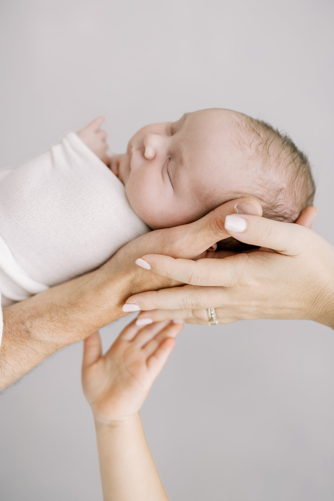 Close-up portrait of a newborn resting peacefully with hands gently supporting the baby's head.