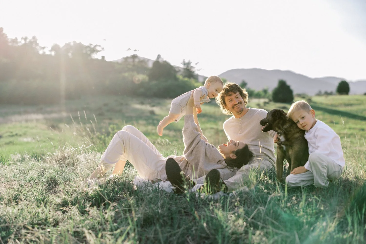 Parents and children relaxing and playing together in a grassy Colorado field at sunset.