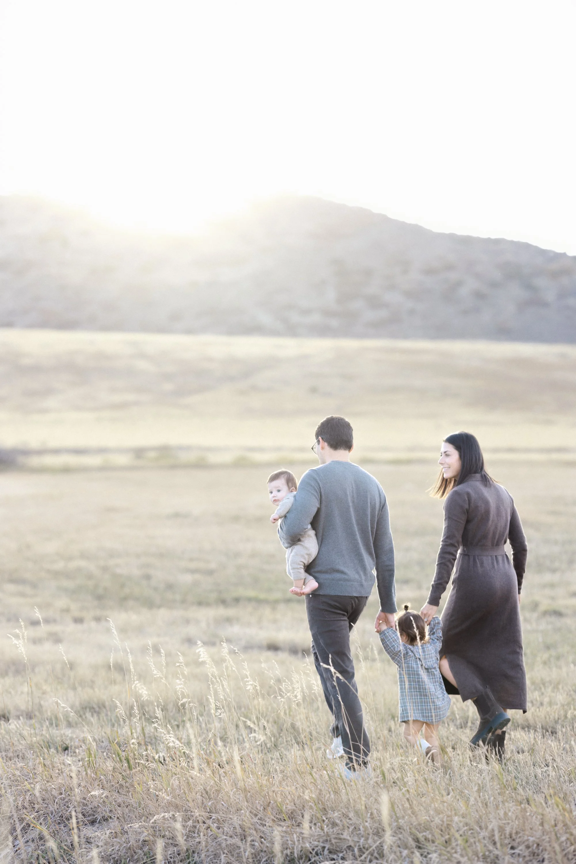 Family walking together through an open field with the Colorado foothills in the distance.