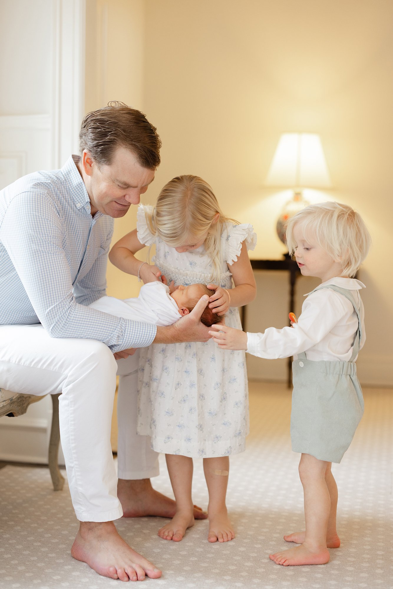 Father holding his newborn while older siblings gather close during a family newborn portrait.