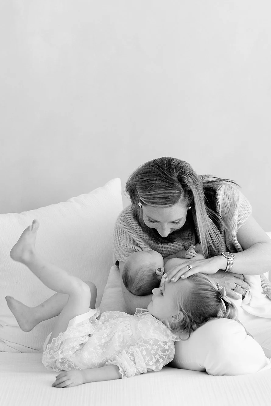 Mother and older siblings cuddling with their newborn on a bed during an in-home newborn photography session.