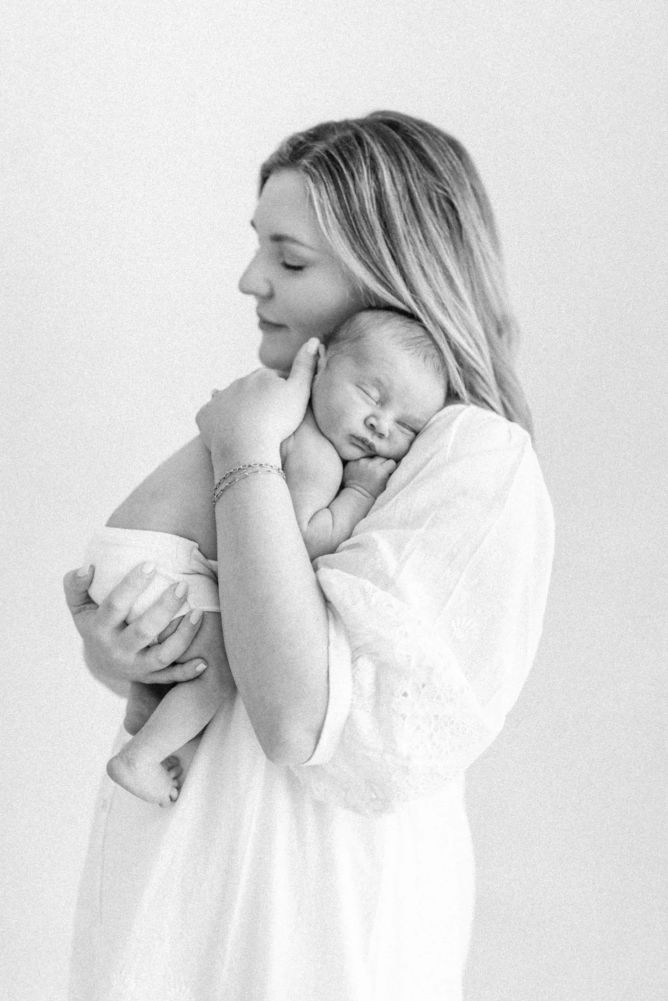 Black and white portrait of a mother gently holding her newborn close during a studio newborn session.