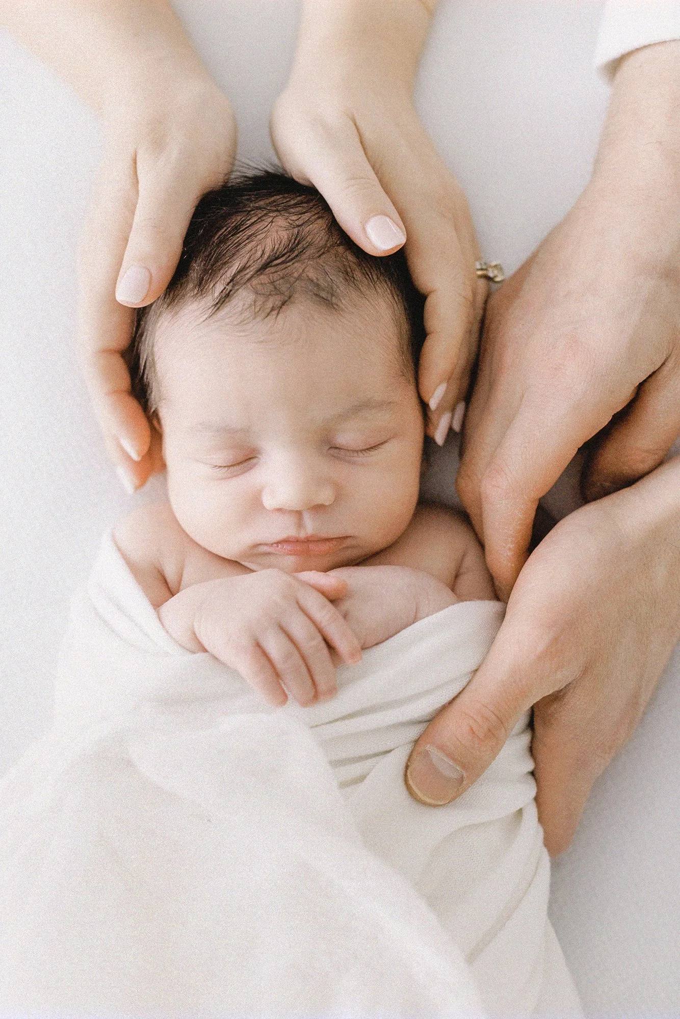 Close-up portrait of a sleeping newborn surrounded by the gentle hands of both parents during a studio session.