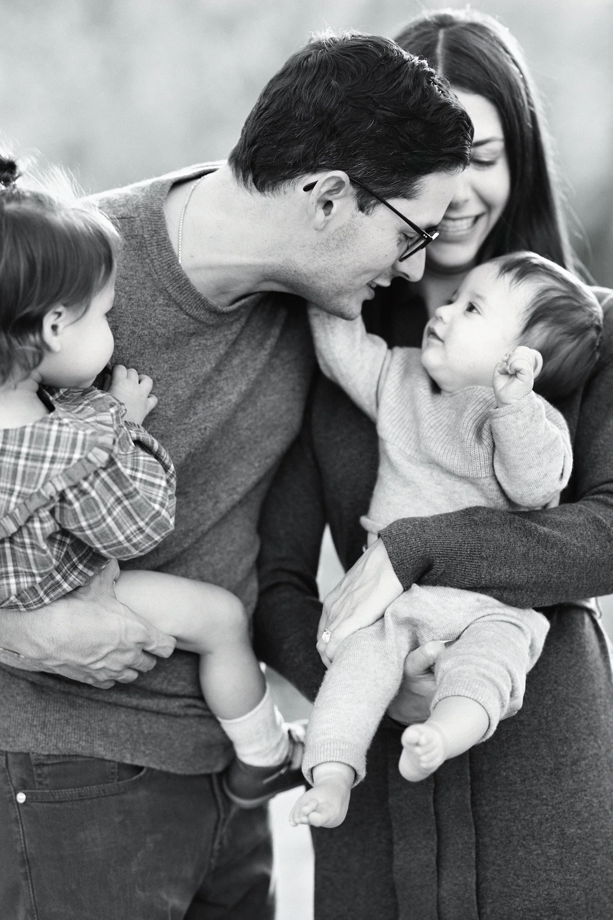 Parents sharing an affectionate moment while holding their two young children.