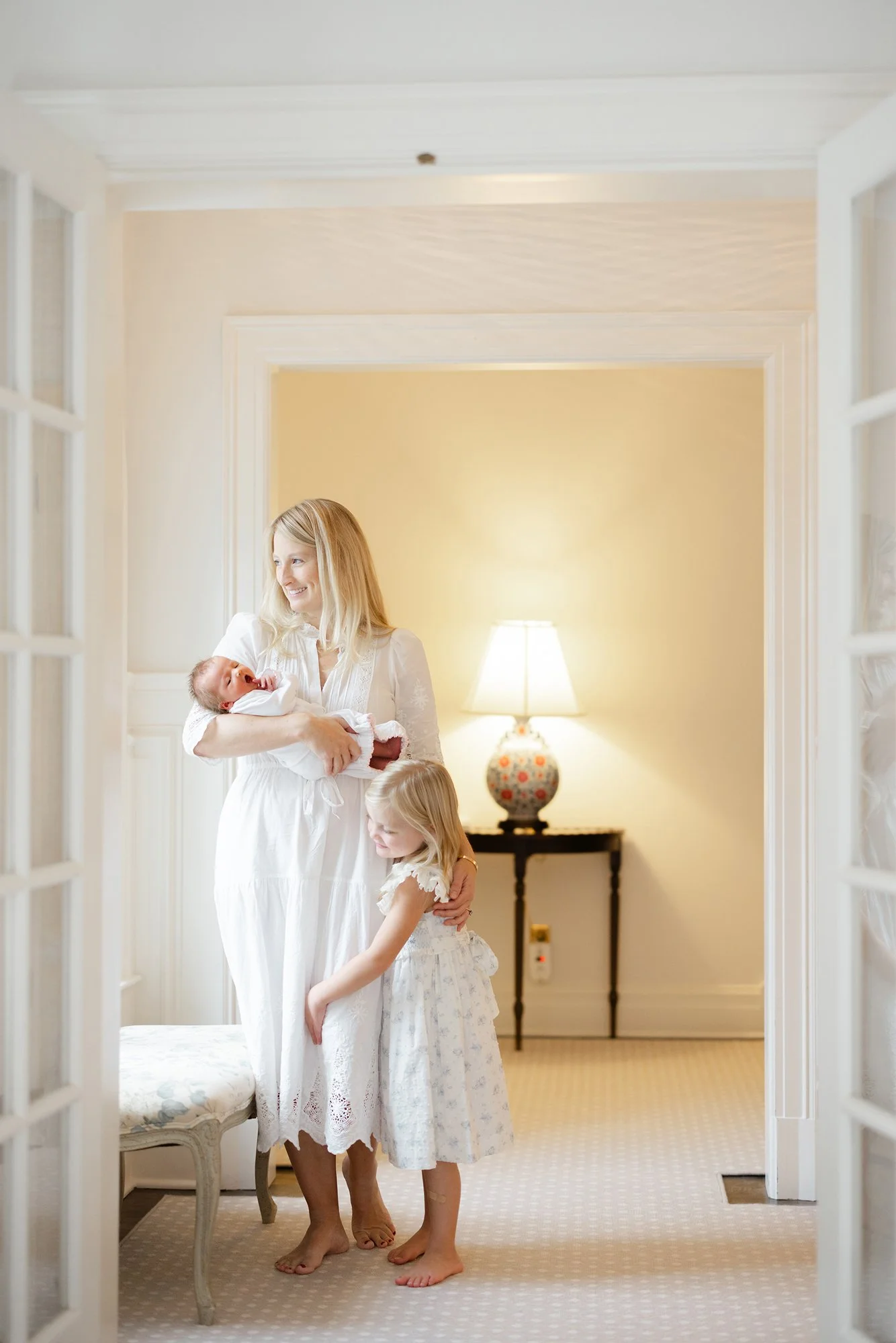 Mother carrying her newborn through a softly lit hallway during an in-home newborn session.