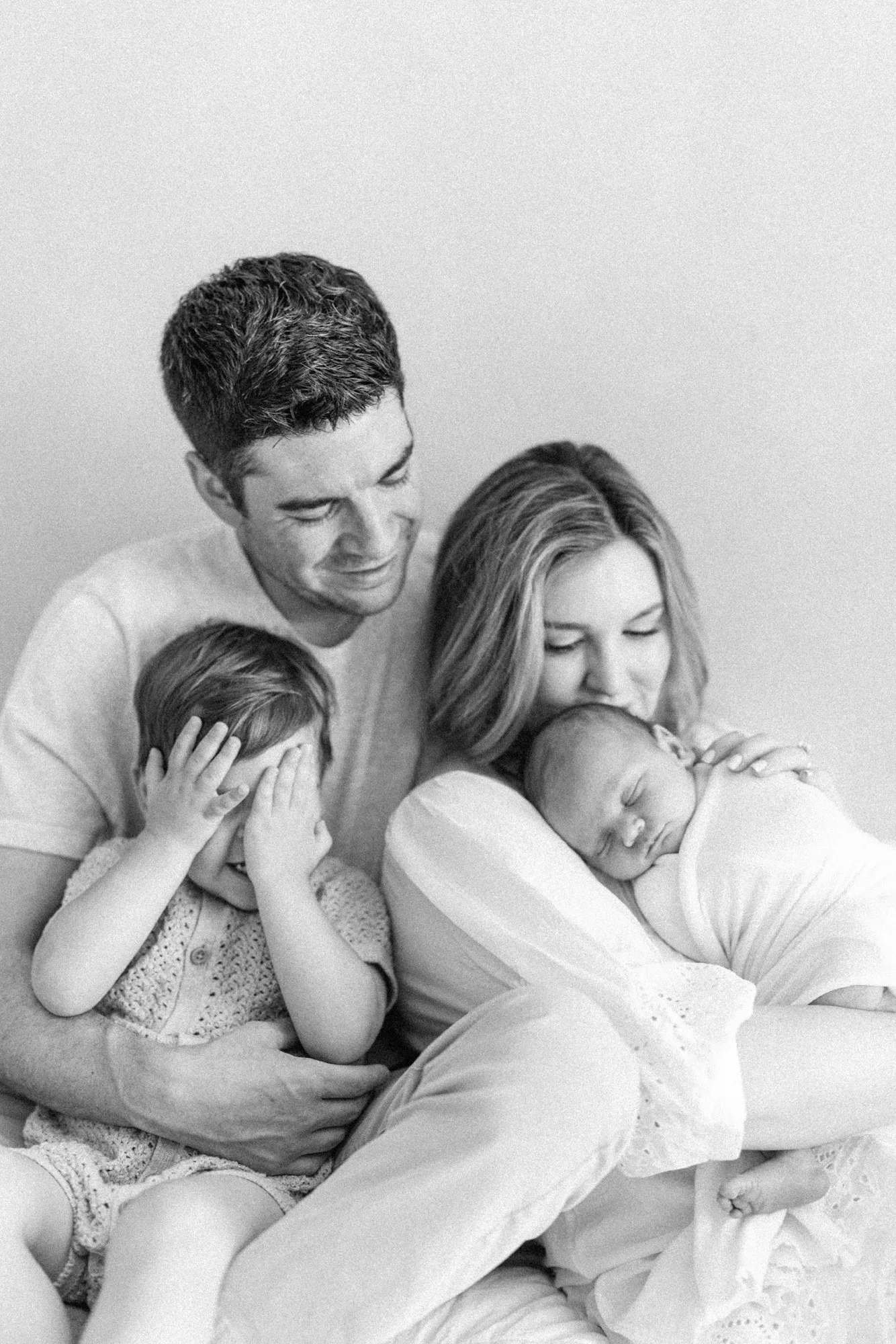 Black and white portrait of parents cuddling together with their newborn and toddler during a studio session.