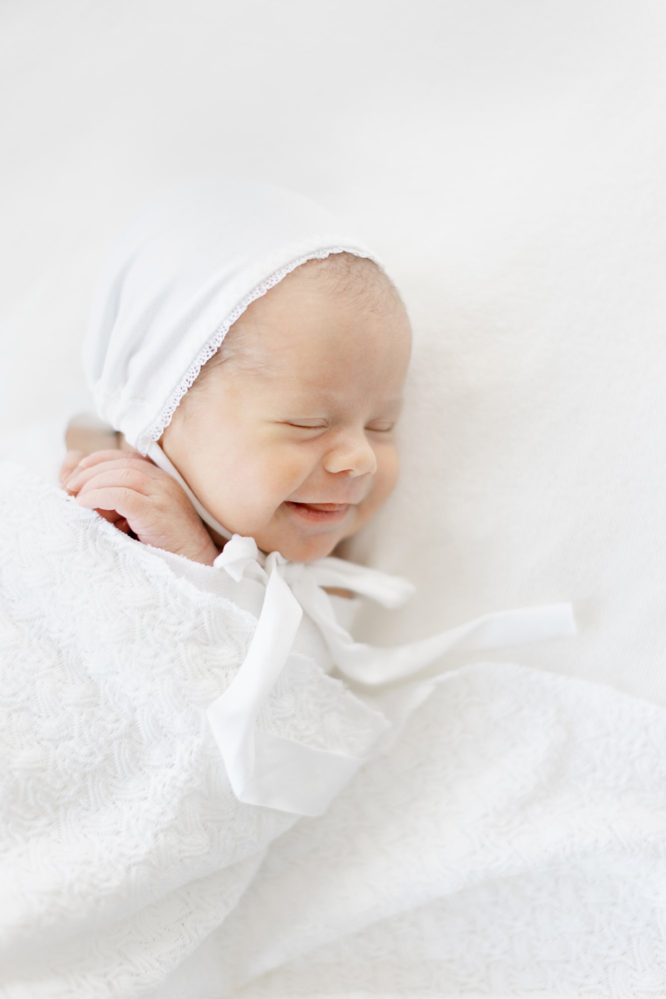 Swaddled newborn baby sleeping with a gentle smile on a soft white blanket during a studio newborn session.