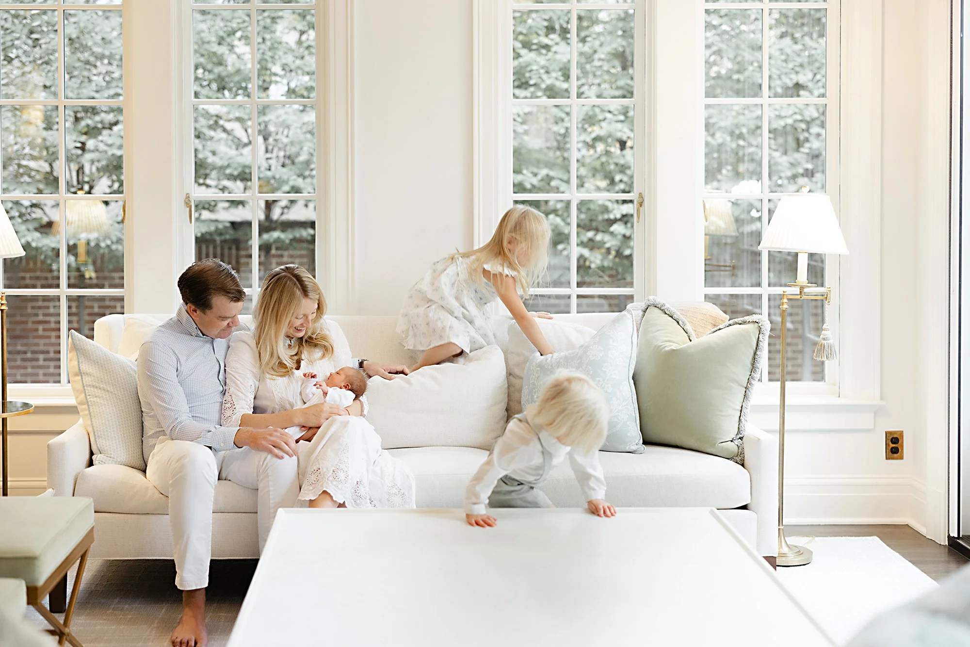 Family relaxing together in a bright living room during an in-home newborn photography session.