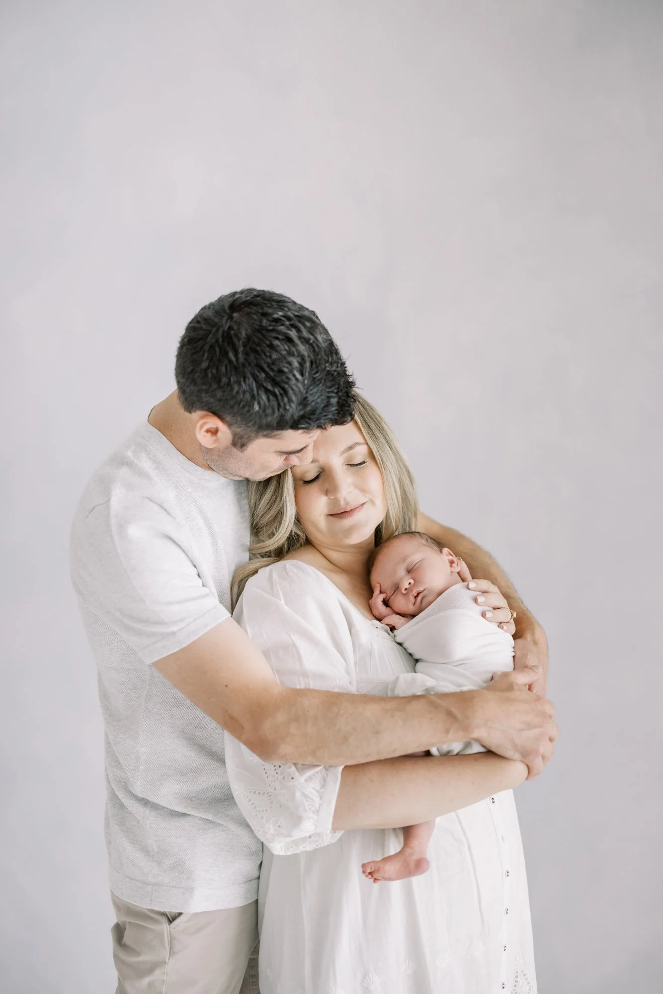 Father embracing mother and newborn during a heartfelt studio family photography session.