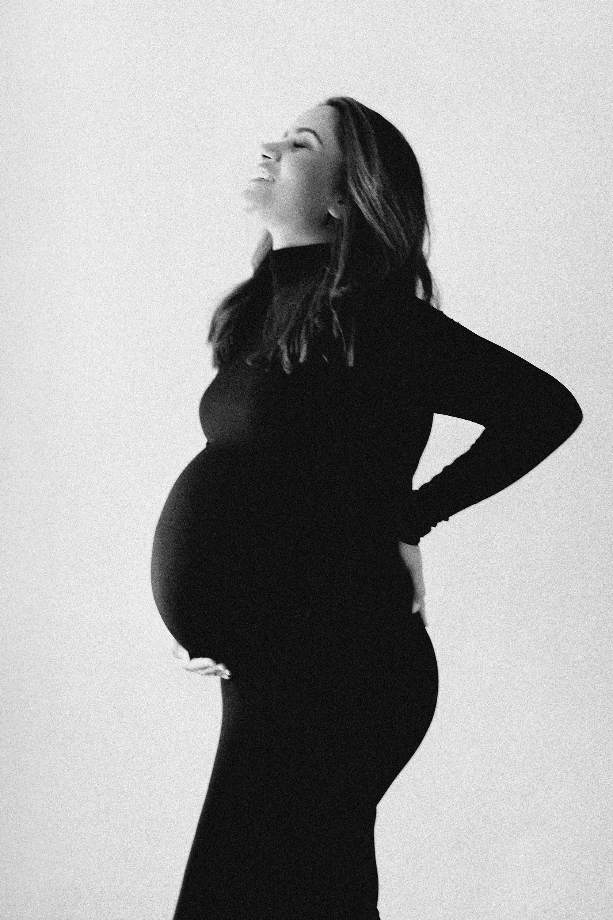 Black and white profile portrait of a pregnant woman wearing a fitted black dress.