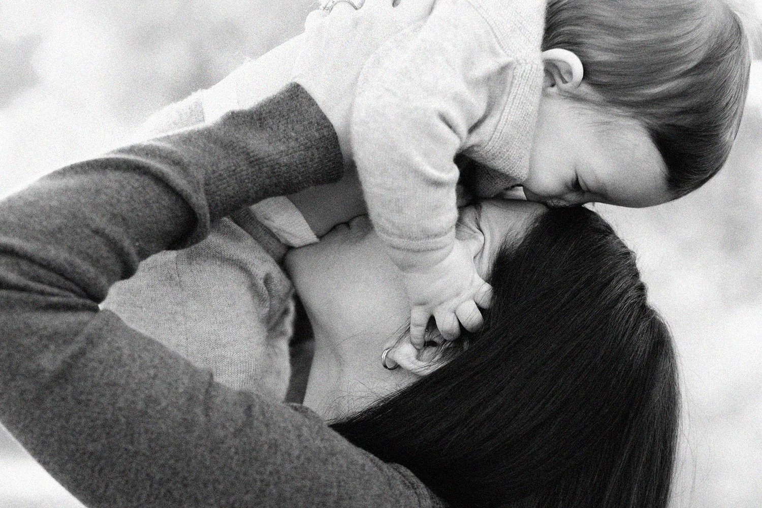 Mother kissing her baby in a close, candid black and white family portrait.