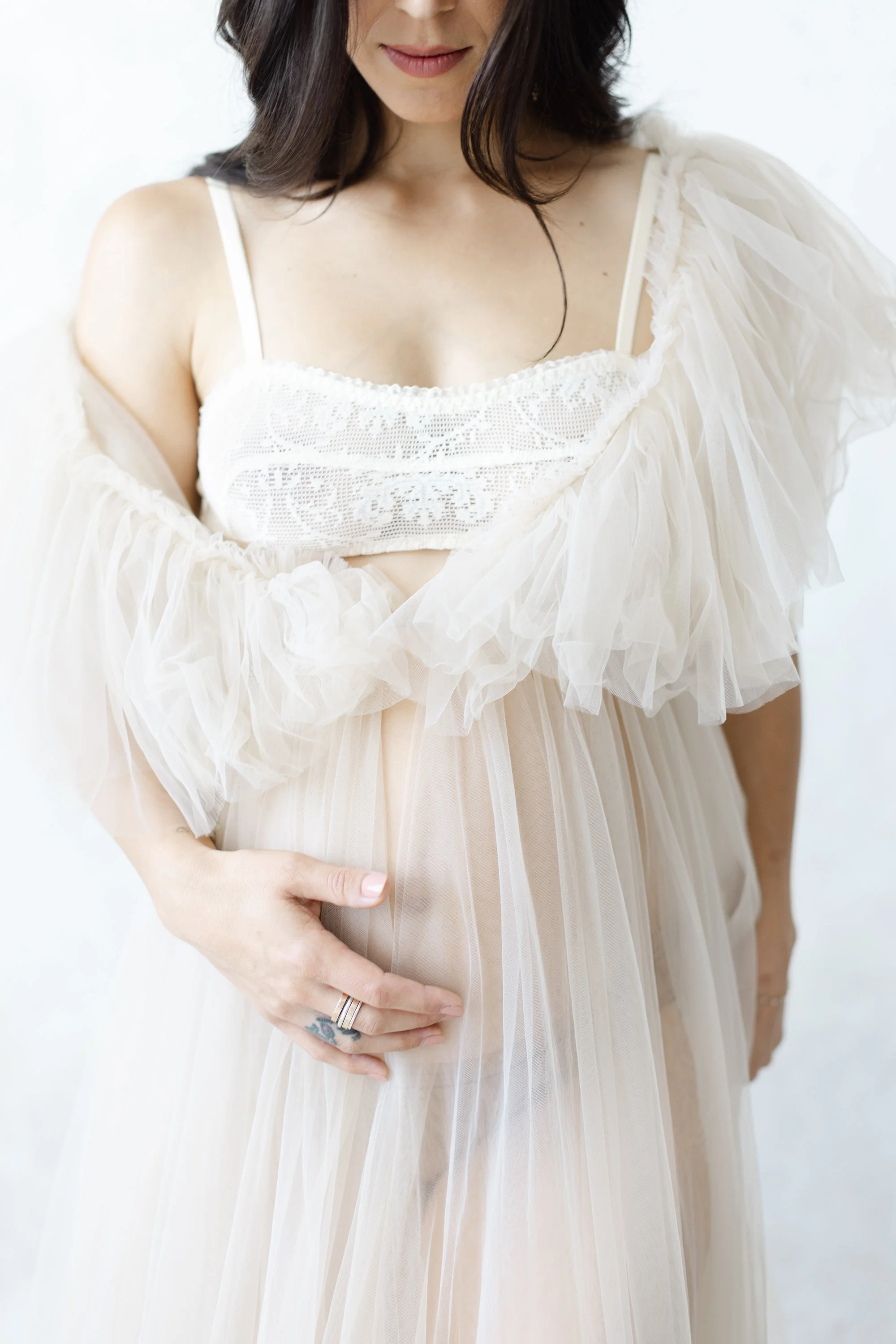 Close-up maternity portrait of a pregnant woman wearing a soft tulle wrap over a white dress.